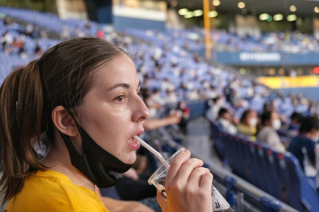 Claire profite d'une boisson pour enlever son masque mais reste captivée par le match