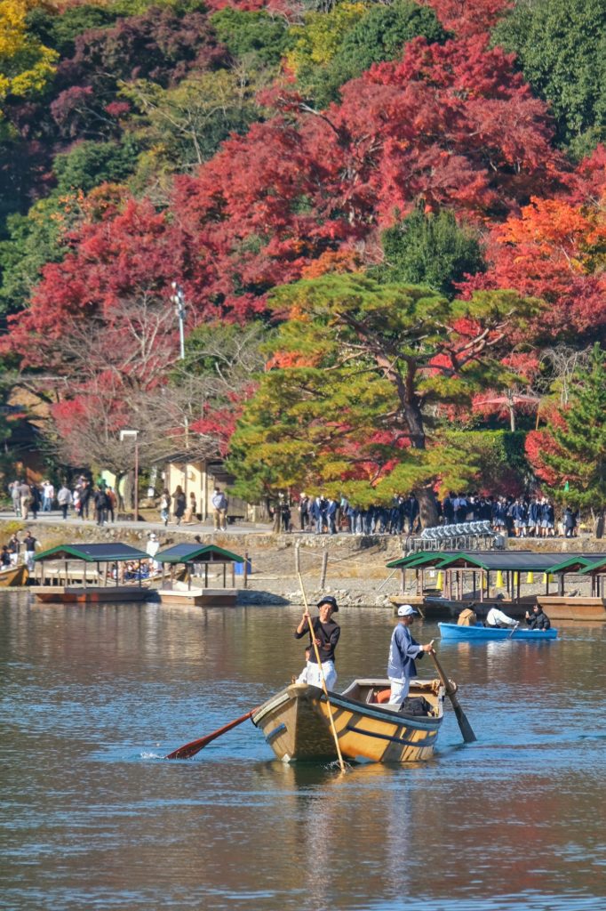 Un bateau sur la rivière Katsura devant les couleurs d'automne du parc Arashiyama