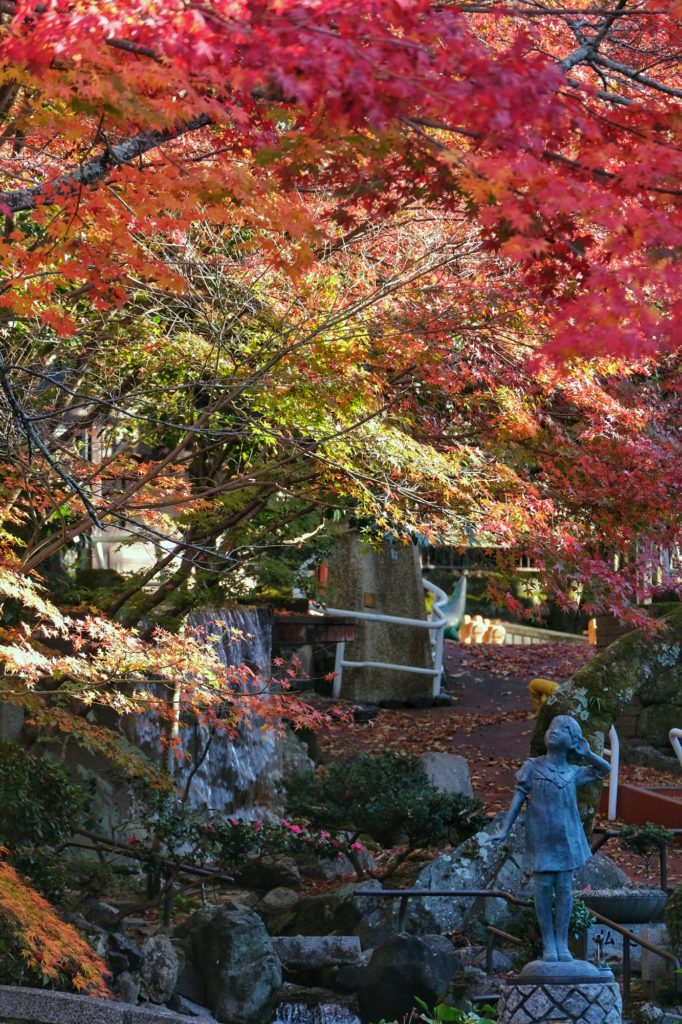 Une statuette de petite fille contemple les érables rouges et orange du Eikan-do Zenrin-ji